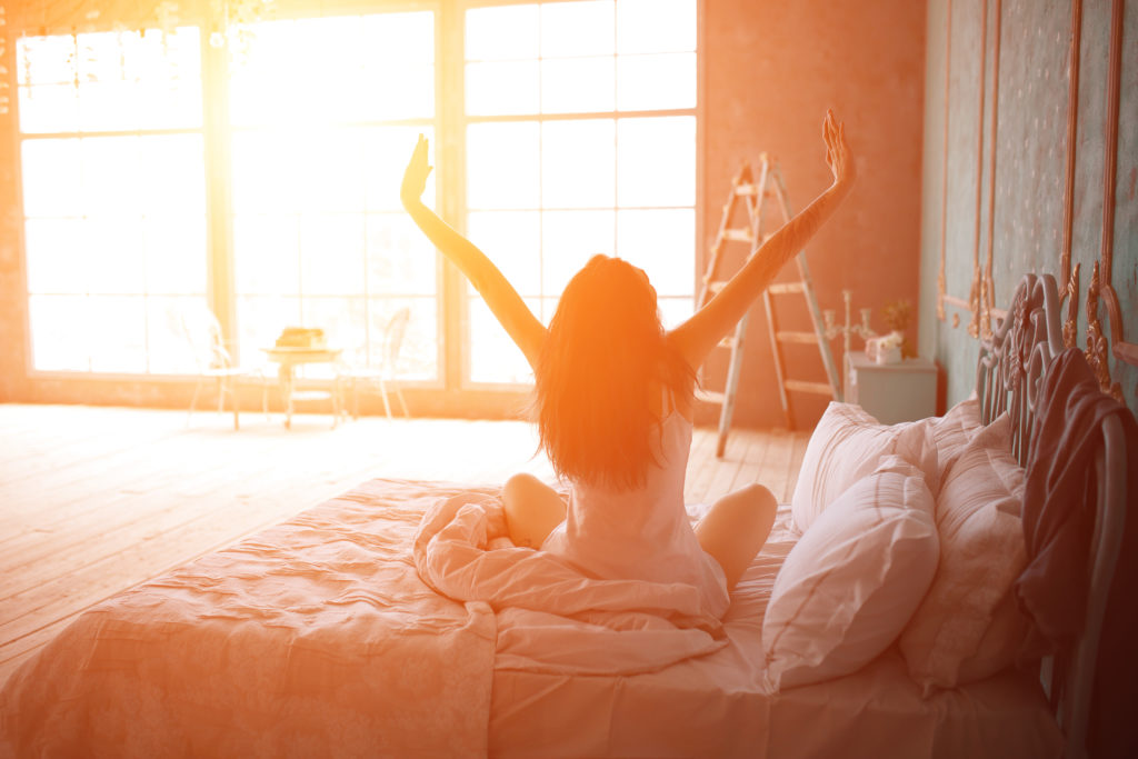 Woman stretching in bed after wake up, back view